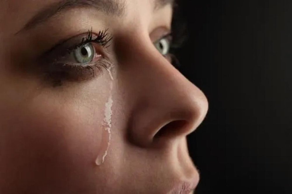 Retrato de una mujer con lágrimas en su rostro, mostrando una profunda expresión emocional. La imagen destaca sus ojos verdes y el contraste de su piel con un fondo oscuro, capturando un momento de vulnerabilidad y sensibilidad. Representa lo que causa acumular emociones reprimidas.