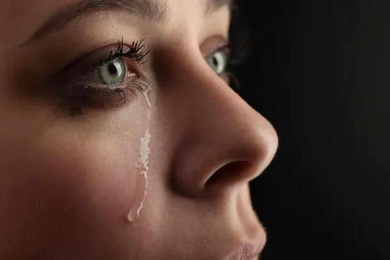 Retrato de una mujer con lágrimas en su rostro, mostrando una profunda expresión emocional. La imagen destaca sus ojos verdes y el contraste de su piel con un fondo oscuro, capturando un momento de vulnerabilidad y sensibilidad. Representa lo que causa acumular emociones reprimidas.