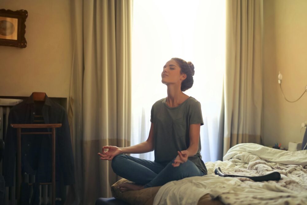 Mujer meditacion sobre su cama sentada expresando una correcta relajacion