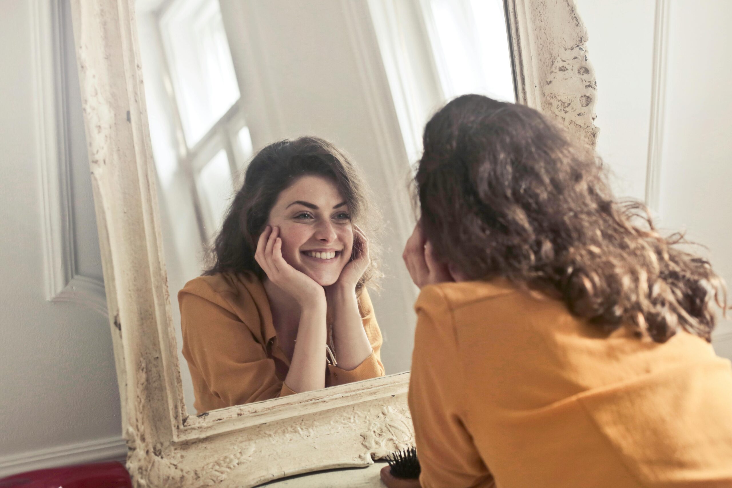 Mujer mirándose al espejo feliz, conforme con su cara demostrando autoestima
